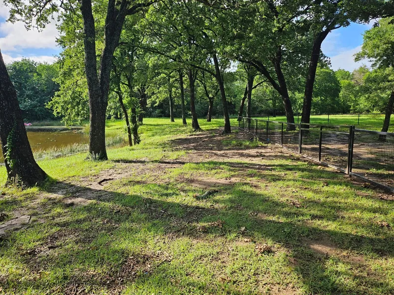 Mowed grass along a wooded, fenced property with a pond